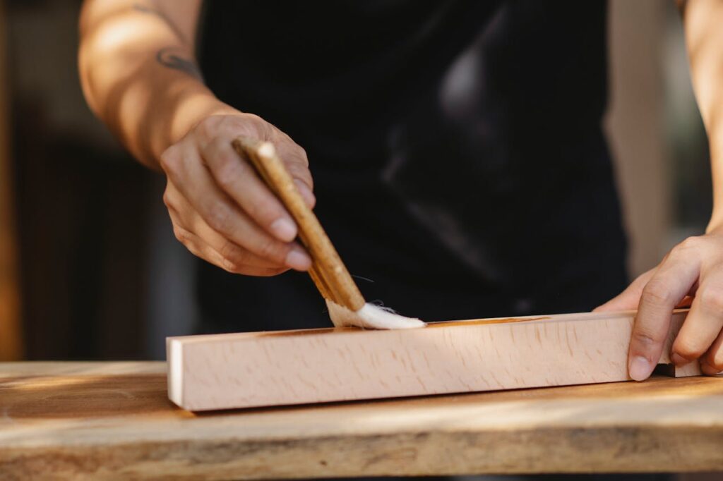 A male craftsman carefully applies varnish to a wooden surface, showcasing artisanal skill.